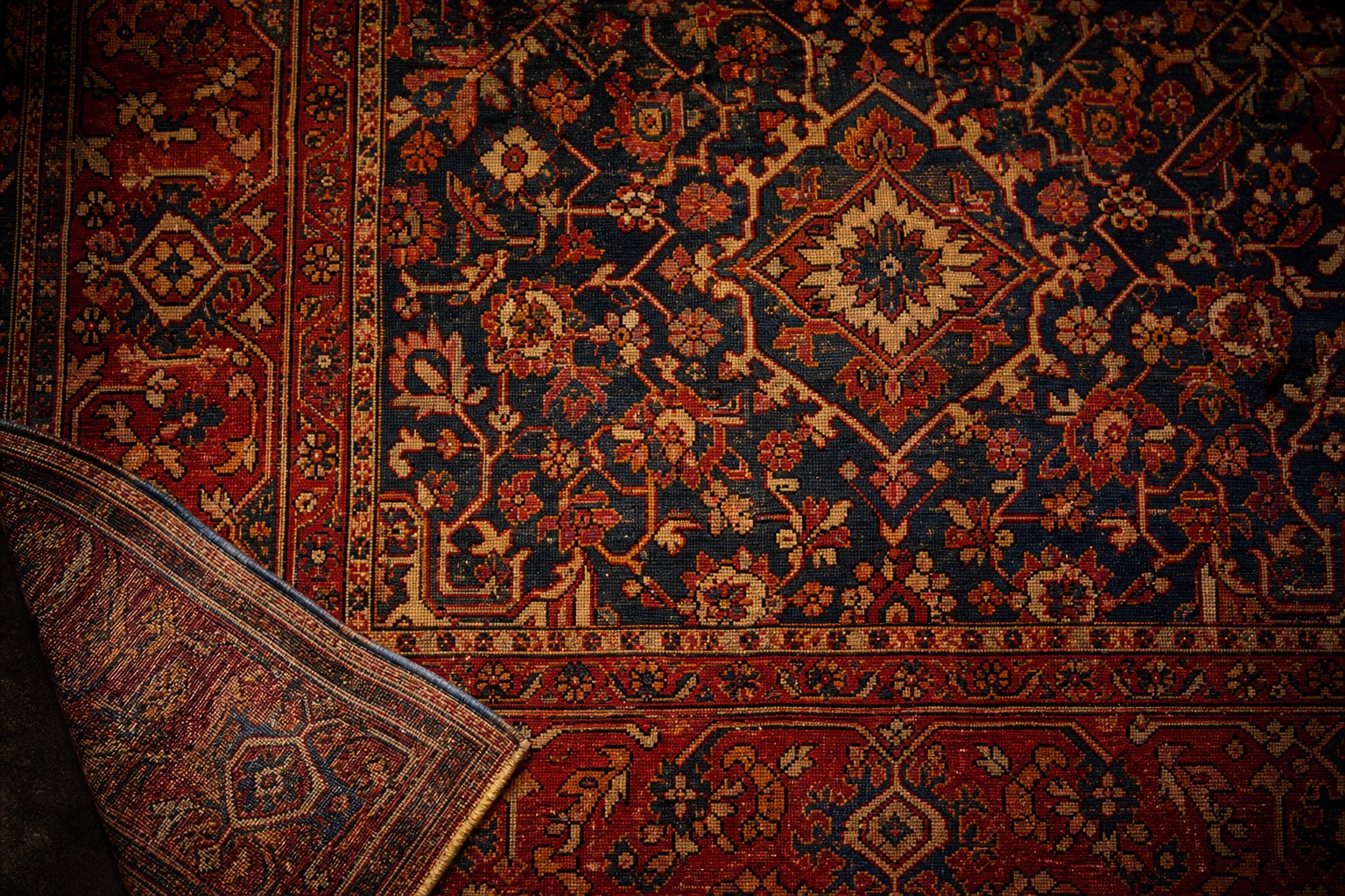 An antique hand-knotted Persian rug with a central medallion, one corner turned back to show the knots